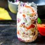 Haitian pikliz Recipe in a clear mason jar with red bell pepper in the back, yellow pepper and black bowl in the background.
