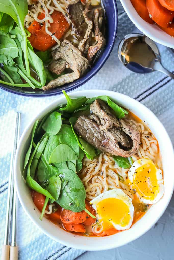 Beef, noodles, spinach, carrots, and soft boiled eggs in broth in white bowl. Full recipe at www.savorythoughts.com