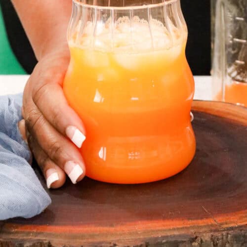 hand holding a glass filled with carrot ginger juice on a wooden board