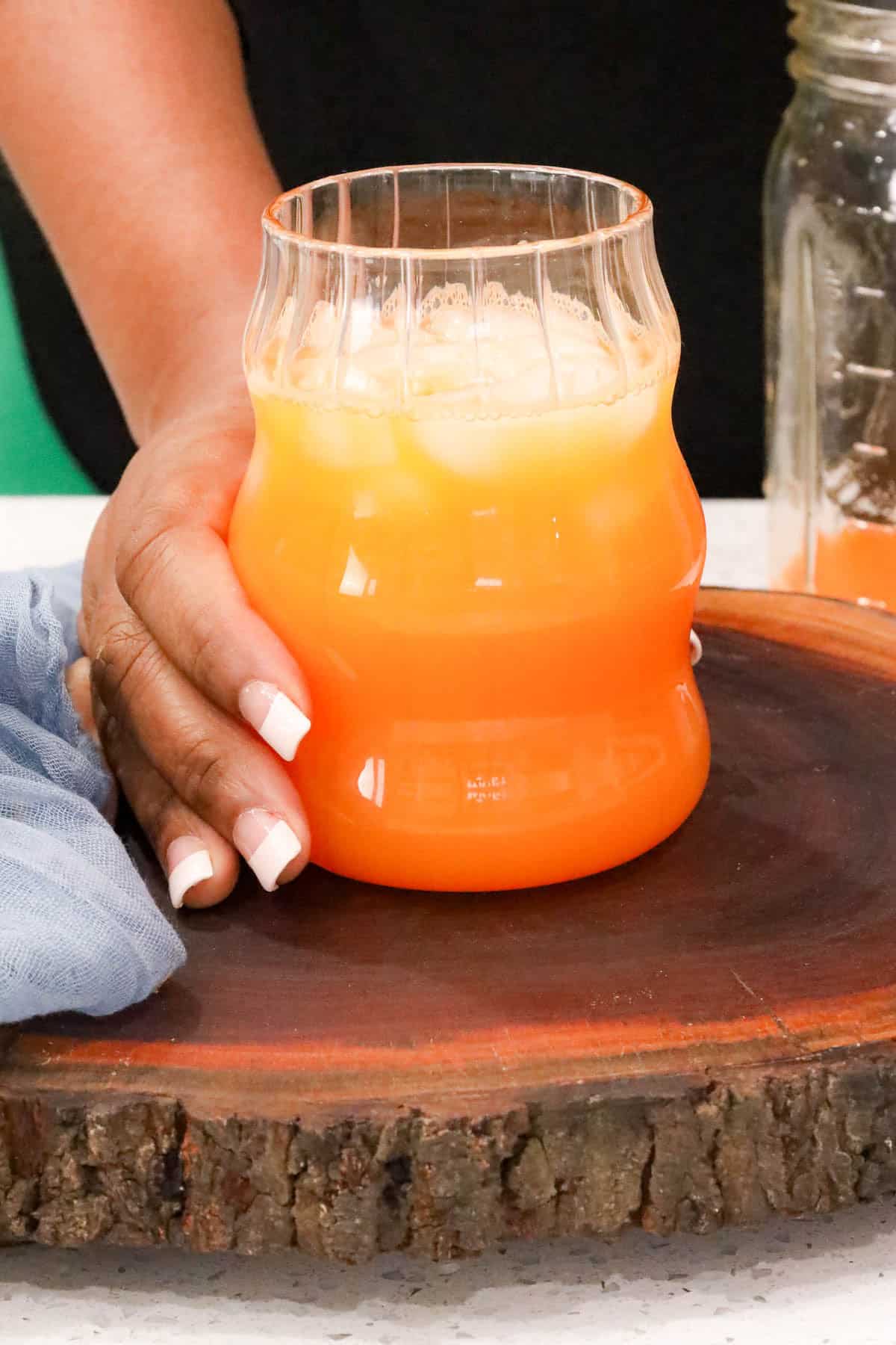 hand holding a glass filled with carrot ginger juice on a wooden board