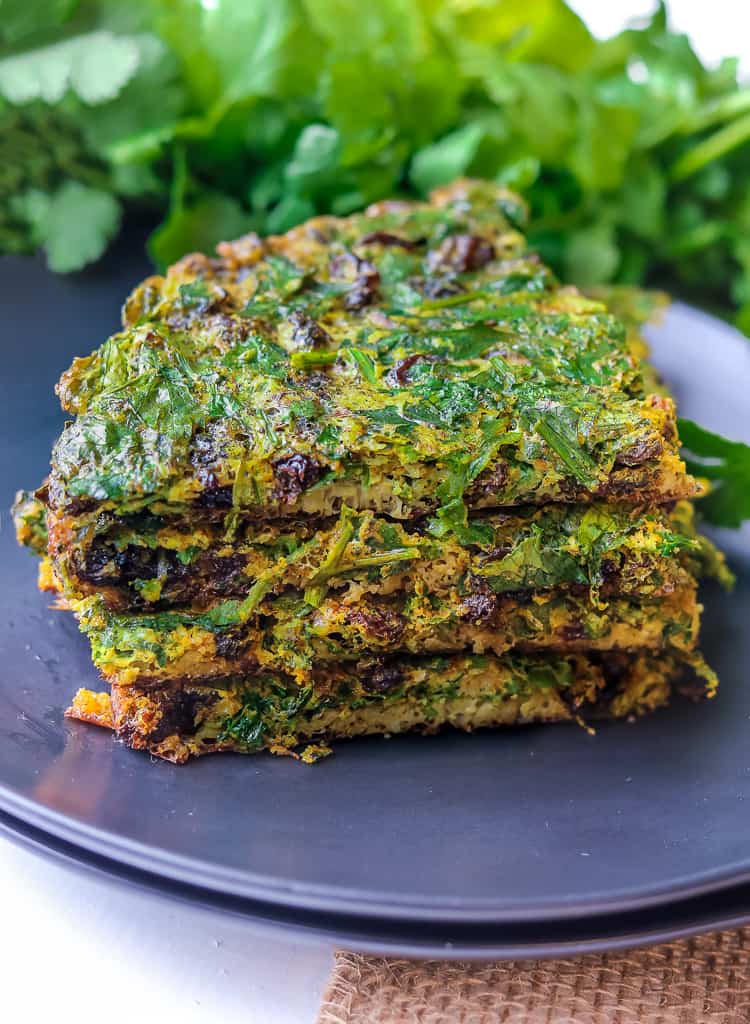 Layered Kuku Sabzi – Persian Herb on a black plate with fresh herbs in the background