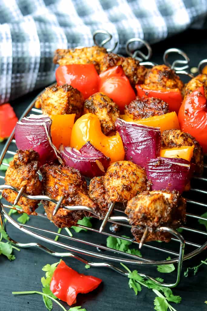 A row of air fryer chicken fajita skewers. threaded with chicken breast, red onions, red bell peppers, and yellow bell peppers.