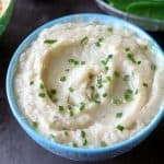 Cauliflower Mashed Potatoes Recipe in a blue bowl topped with chives. This Mashed Cauliflower Instant Pot recipe is epic! Made with sautéed garlic. Easy low carb side dish! Creamy and scrumptious gluten-free Instant Pot Cauliflower.