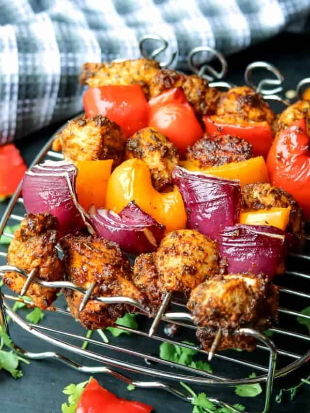 A row of air fryer chicken fajita skewers. threaded with chicken breast, red onions, red bell peppers, and yellow bell peppers.