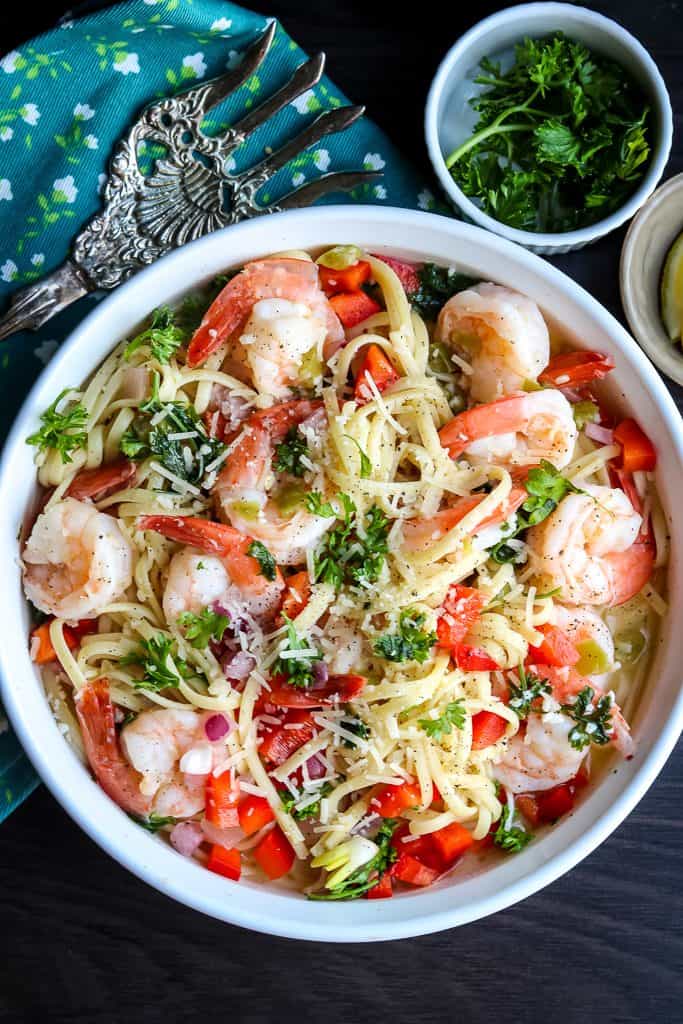 Creamy shrimp scampi on a white dish topped with fresh parsley, tomatoes, and onions.
