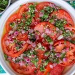 Marinated tomatoes toped with fresh herbs and red onions that's submerged in oil and cooking oil.