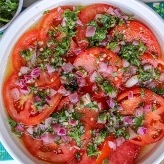 Marinated tomatoes toped with fresh herbs and red onions that's submerged in oil and cooking oil.