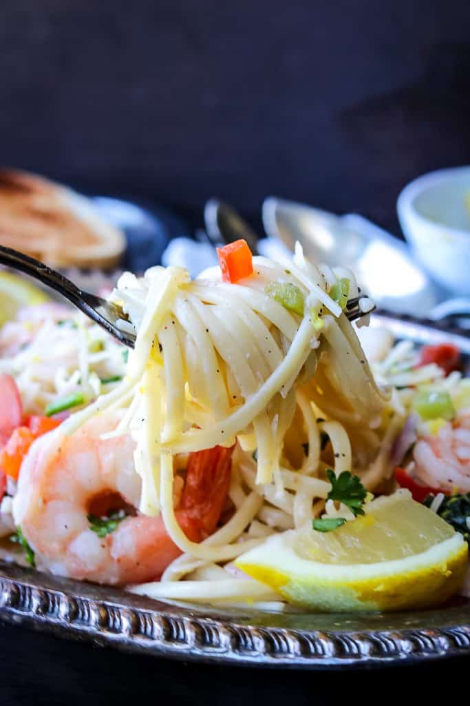 scampi pasta lifted with a fork. Plated with shrimp and lemon