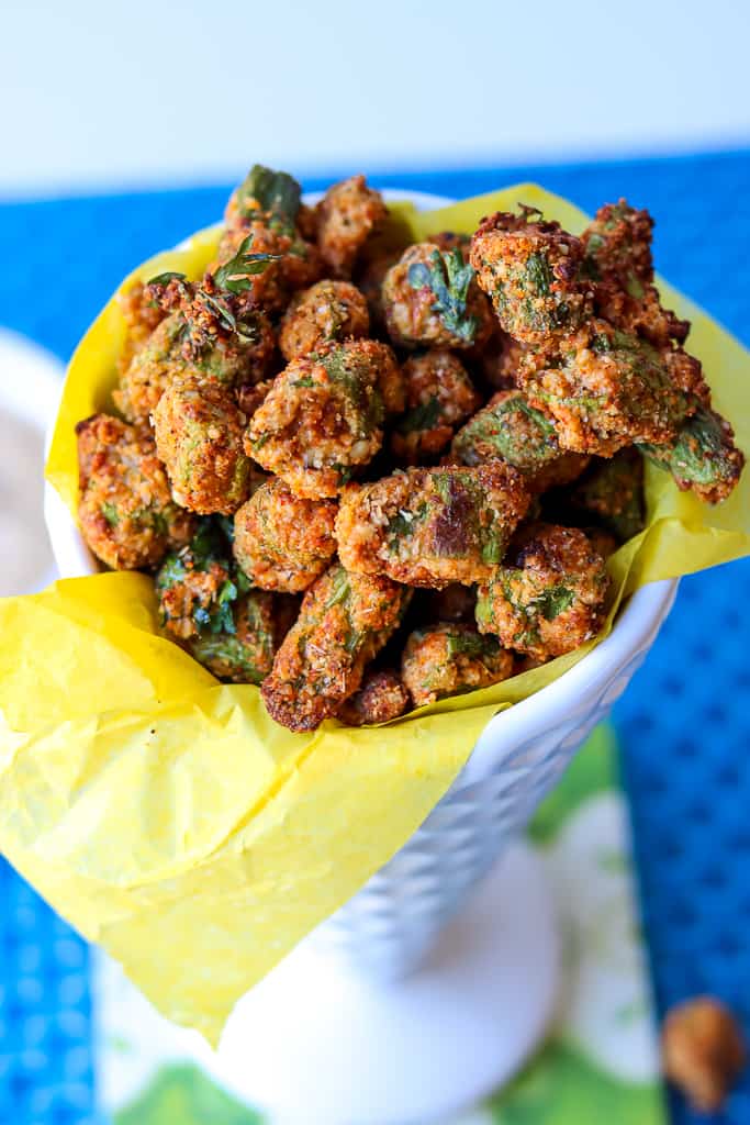 Air fryer okra bites in a white cone cup with yellow lining. Crispy Air Fryer Fried Okra recipe that’s easy to make and fried to a golden crispy texture. A healthier alternative to the traditional deep-fried version. One of the best okra recipes you would want to make. #airfryerfriedokra #airfryerokra #airfriedokra #freshokra #airfryerfrozenokra #friedokrarecipe