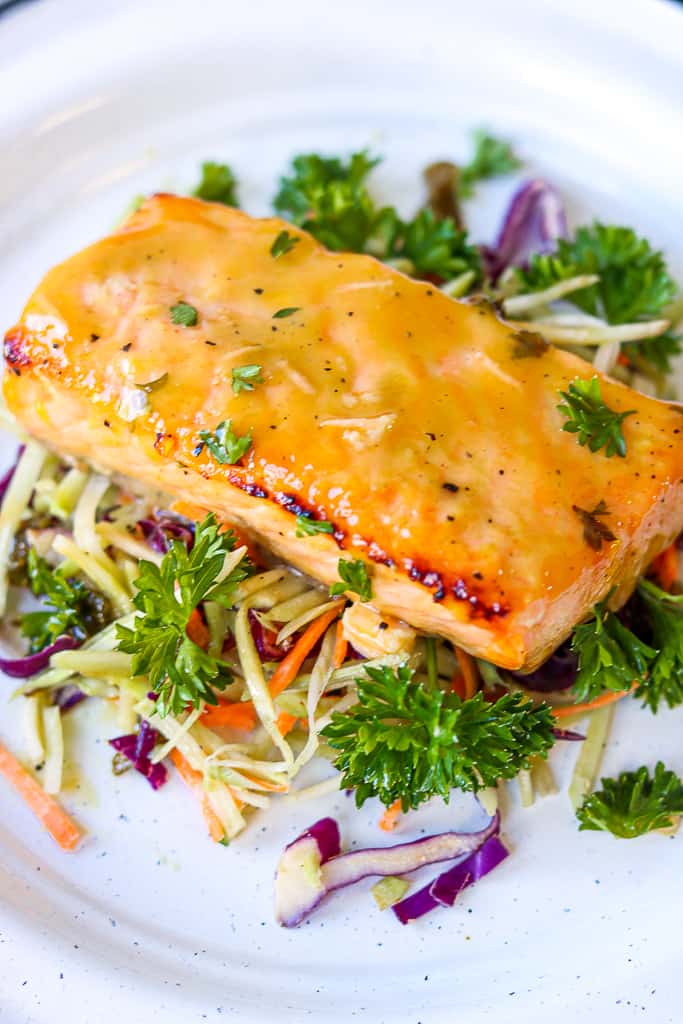 Honey Mustard Glazed Salmon on top of vegetable bed served on a white plate. Honey Mustard Glazed Salmon - Air Fryer Recipe is a quick, easy, and a healthy weeknight dinner. A hearty baked salmon recipe that’s fuss-free! Baked salmon fillet made in the air fryer to perfection. A flavorful simple meal that that’s ready in 10 minutes. #air fryer #honey #mustard #dijonmustard #recipes #paleo #honeymustardglaze #healthy #lemon