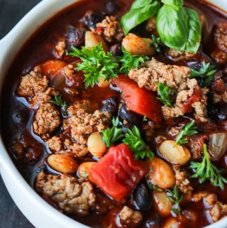 Chili in a white plate topped with fresh herbs and tomatoes