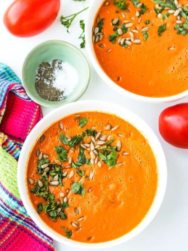 Two bowls of Tomato Carrot Soup topped with chopped fresh herbs and pumpkin seeds