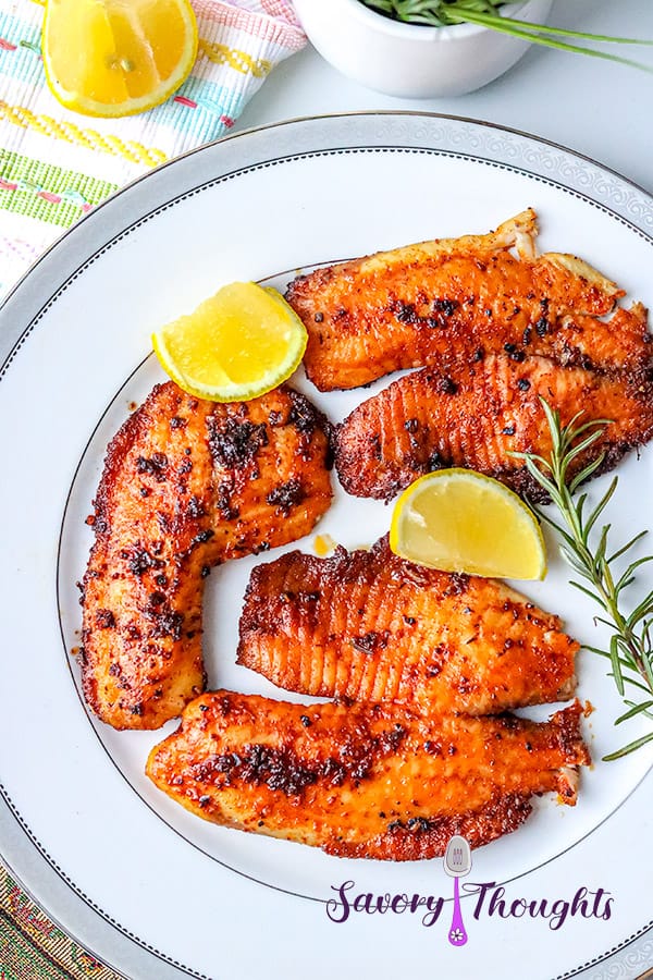 fish on white plate with lemon wedges and rosemary sprig.