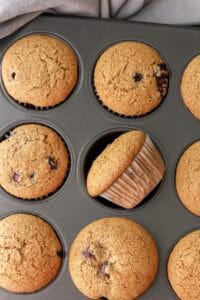 baked blueberry muffins in muffin tray with one laying on the side in the muffin tray cavity