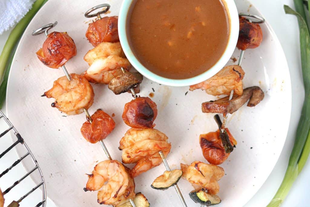 Shrimp threaded on air fryer sticks with mushroom and tomatoes on a plate with peanut sauce