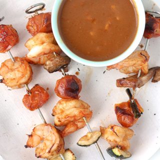 Shrimp threaded on air fryer sticks with mushroom and tomatoes on a plate with peanut sauce