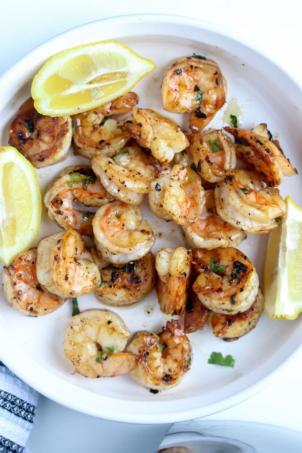 garlic butter shrimp in white plate with lemon wedges