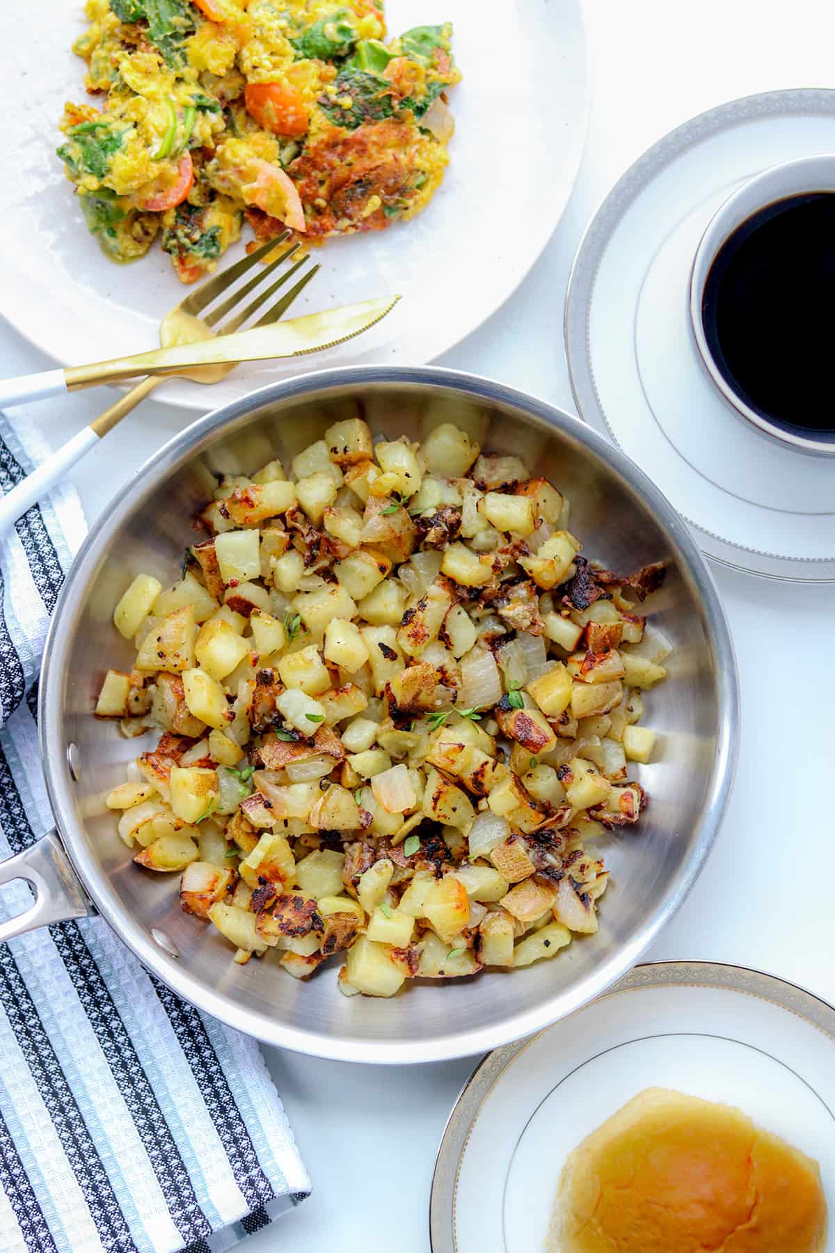 Potatoes in skillet with eggs, bread roll, and coffee