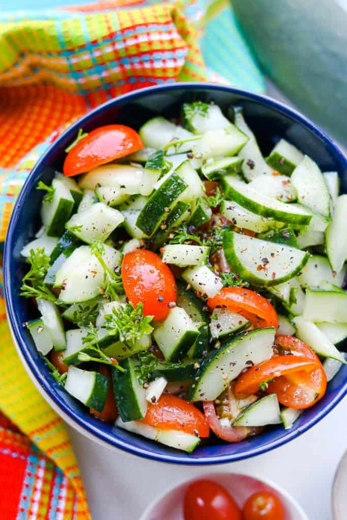 Cucumber Salad In dark blue plate with colorful tablecloth, cherry tomatoes, and cucumber