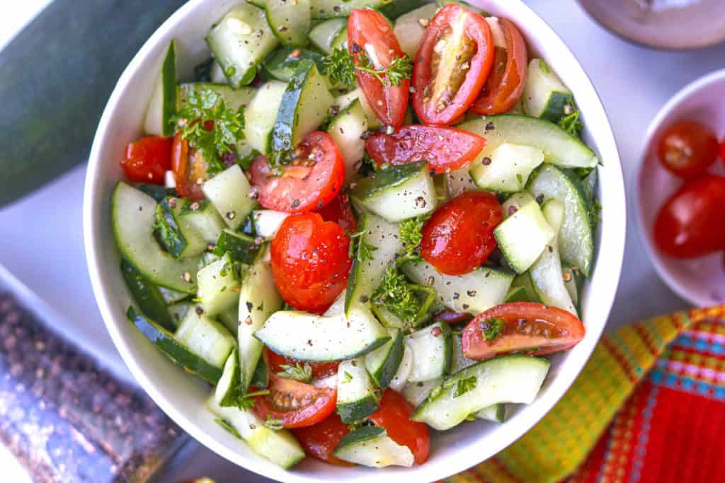 Marinated Cucumber Tomato Salad in white bowl with cherry tomatoes on the side