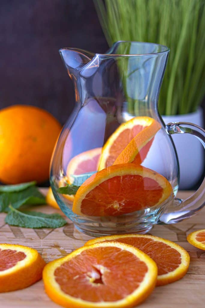 Orange and mint in pitcher with oranges slices on cutting board