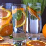orange infused water in glasses and pitcher with orange slices on cutting board