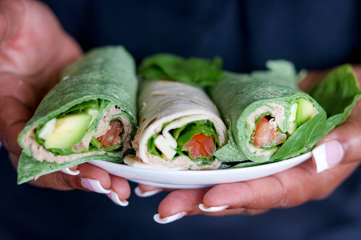 pair of two hands holding tuna wraps on a plate. 