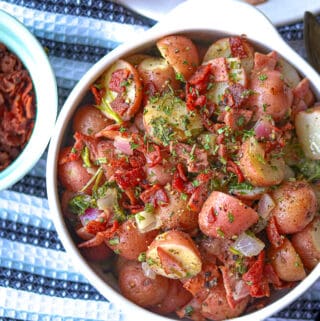 Hot German Style Potato Salad in white bowl on black and white kitchen towel.