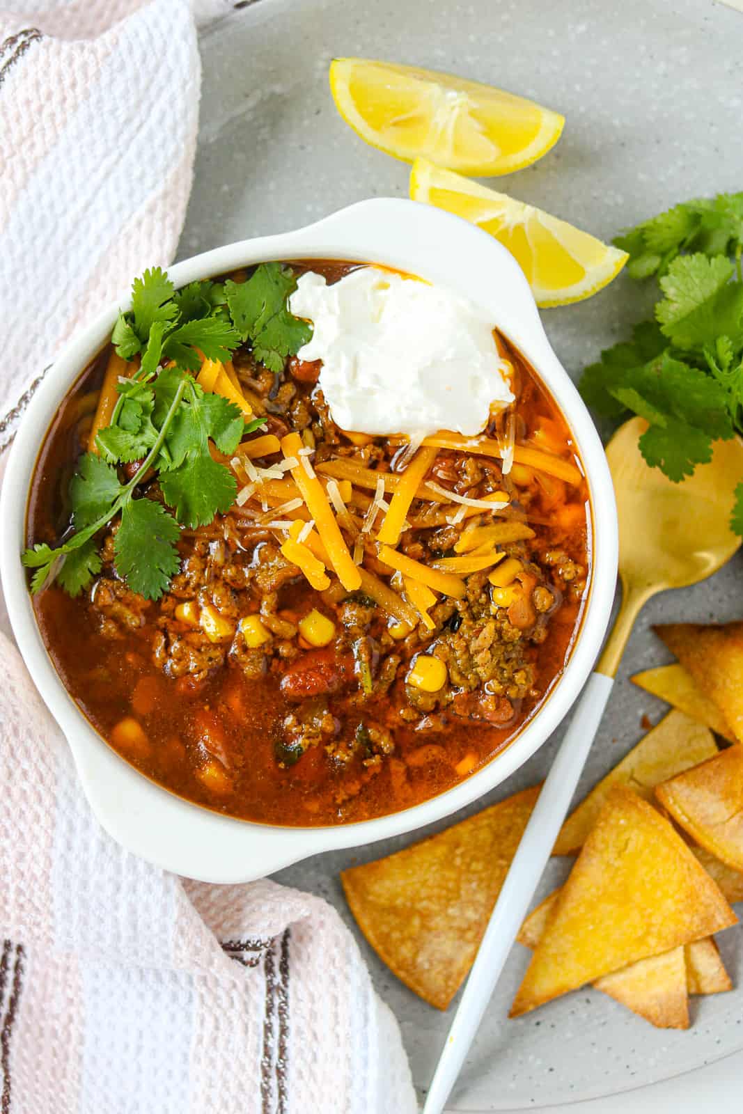 taco soup in white bowl topped with cheese, cilantro on a plate with chips