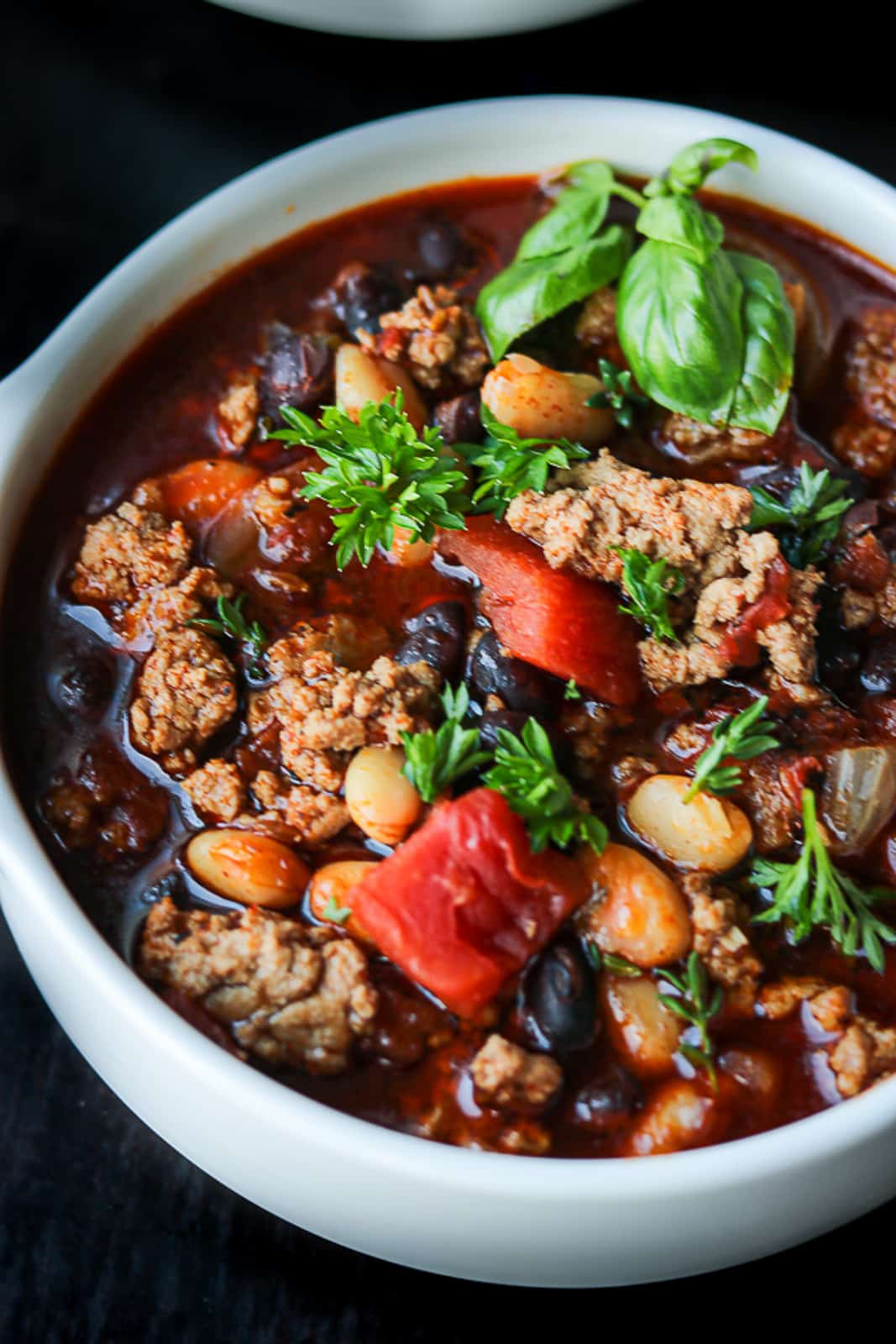 turkey bean soup in white bowl topped with fresh herbs