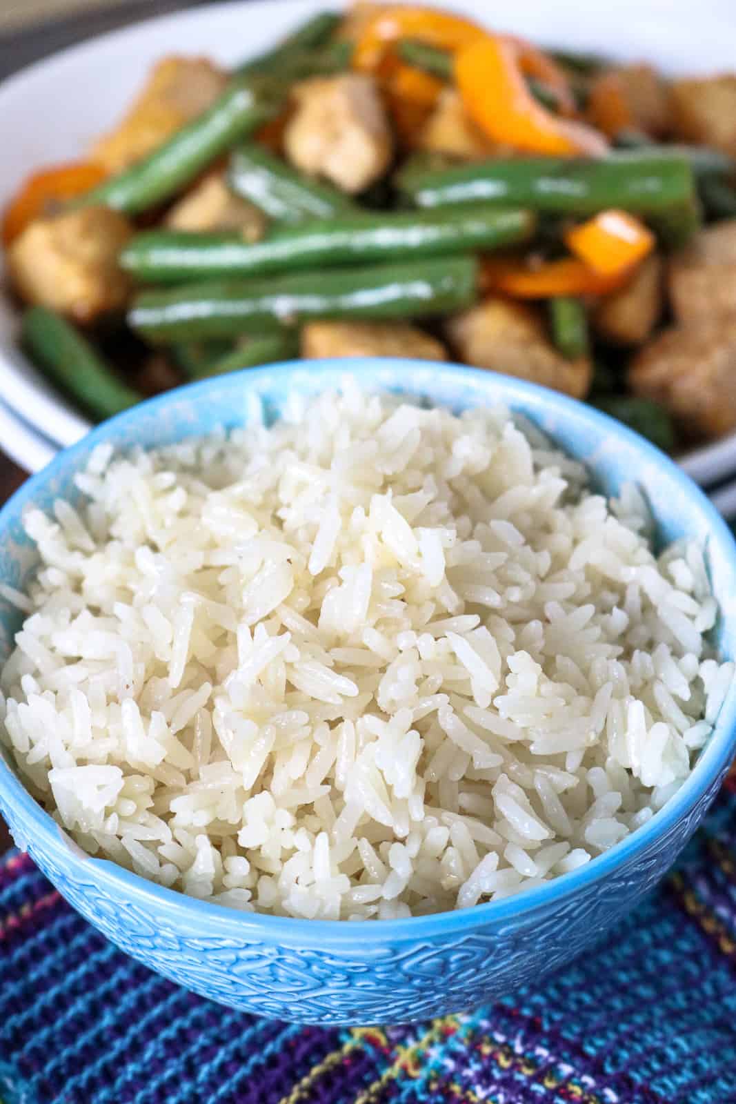 White rice in a blue plate with green beans tofu in the background