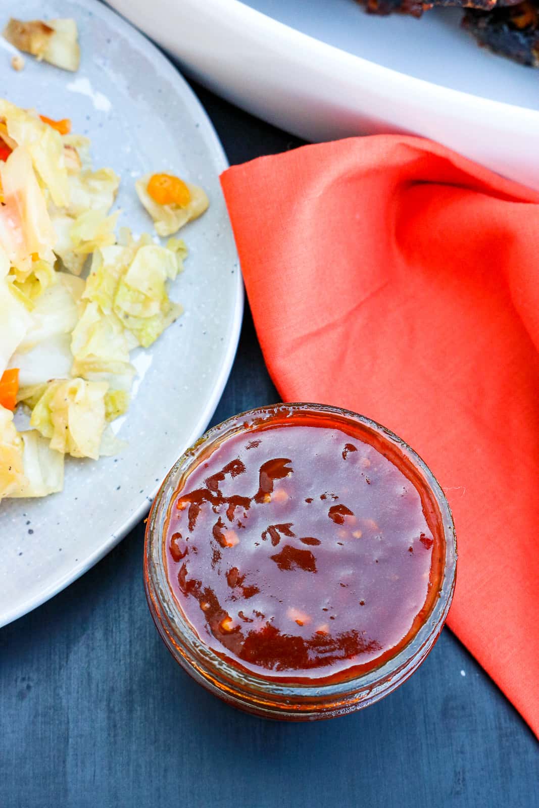 Red savory sauce in glass jar on back table with veggies in the background