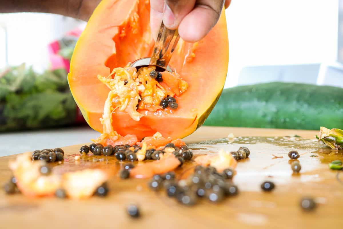 Papaya being scrapped outwith spoon on cutting board.