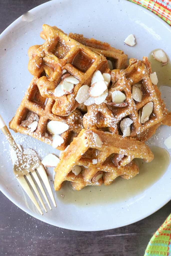 Pieces of waffles on gray plate topped with walnuts and syrup. 