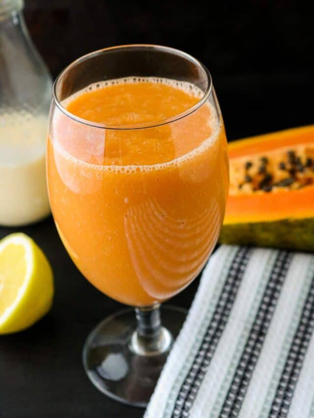 Juice in glass on blackboard with papaya in the background, including milk, lemon juice