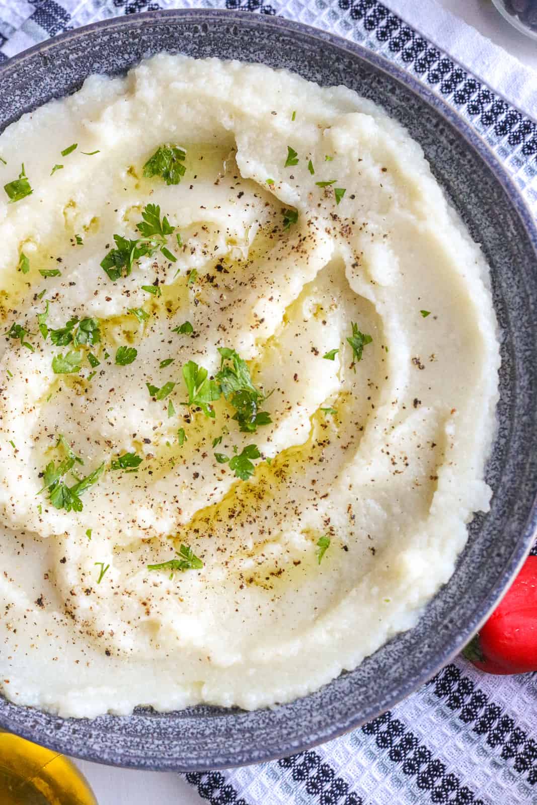 Cauliflower in mashed formed in gray bowl. topped with herbs and olive oil.