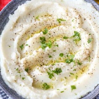 cauliflower in mashed formed in gray bowl. topped with herbs and olive oil.