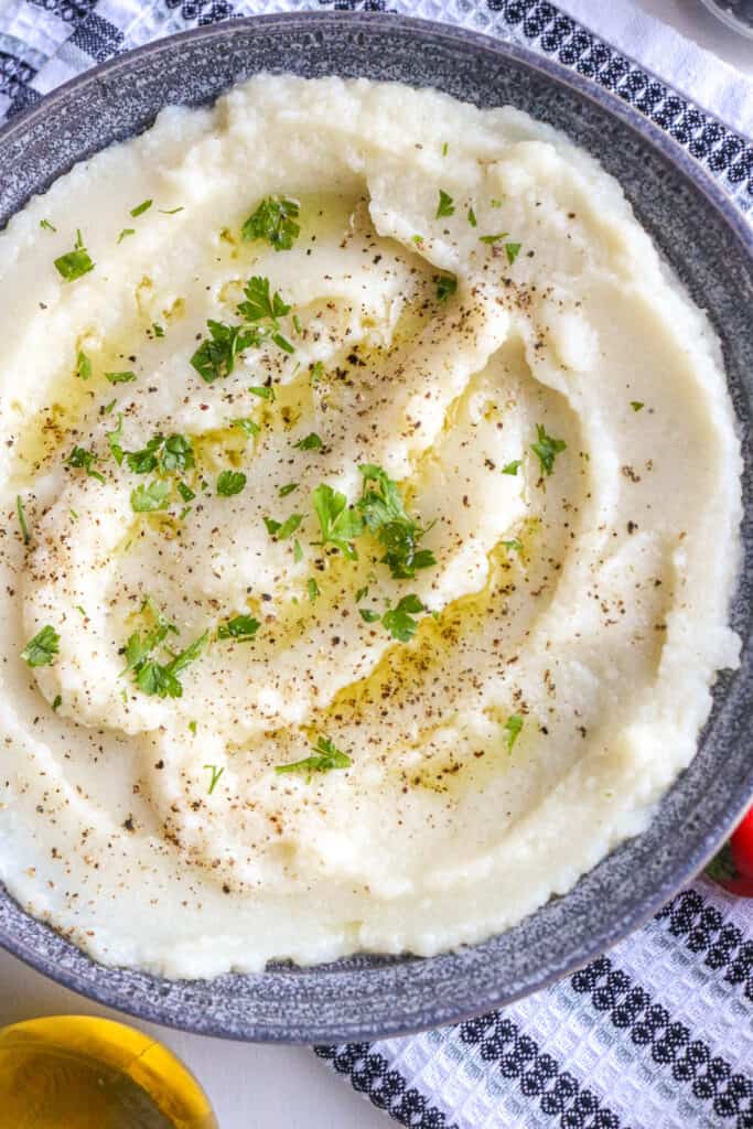 Instant Pot Cauliflower In gray bowl topped with herbs and olive oil