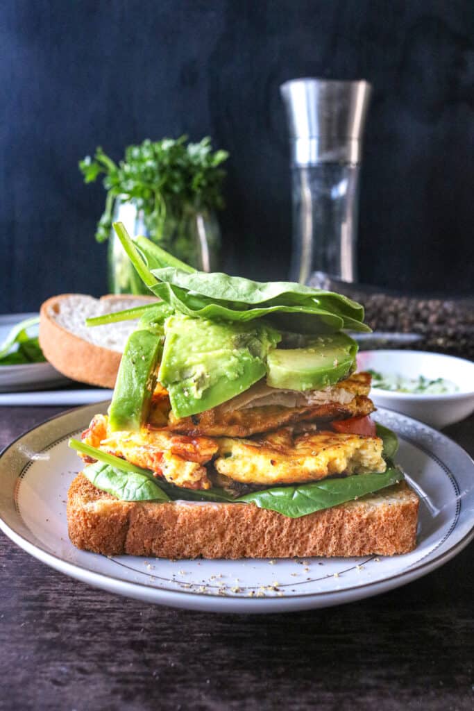 egg sandwich stacked with spinach, avocado, and meat