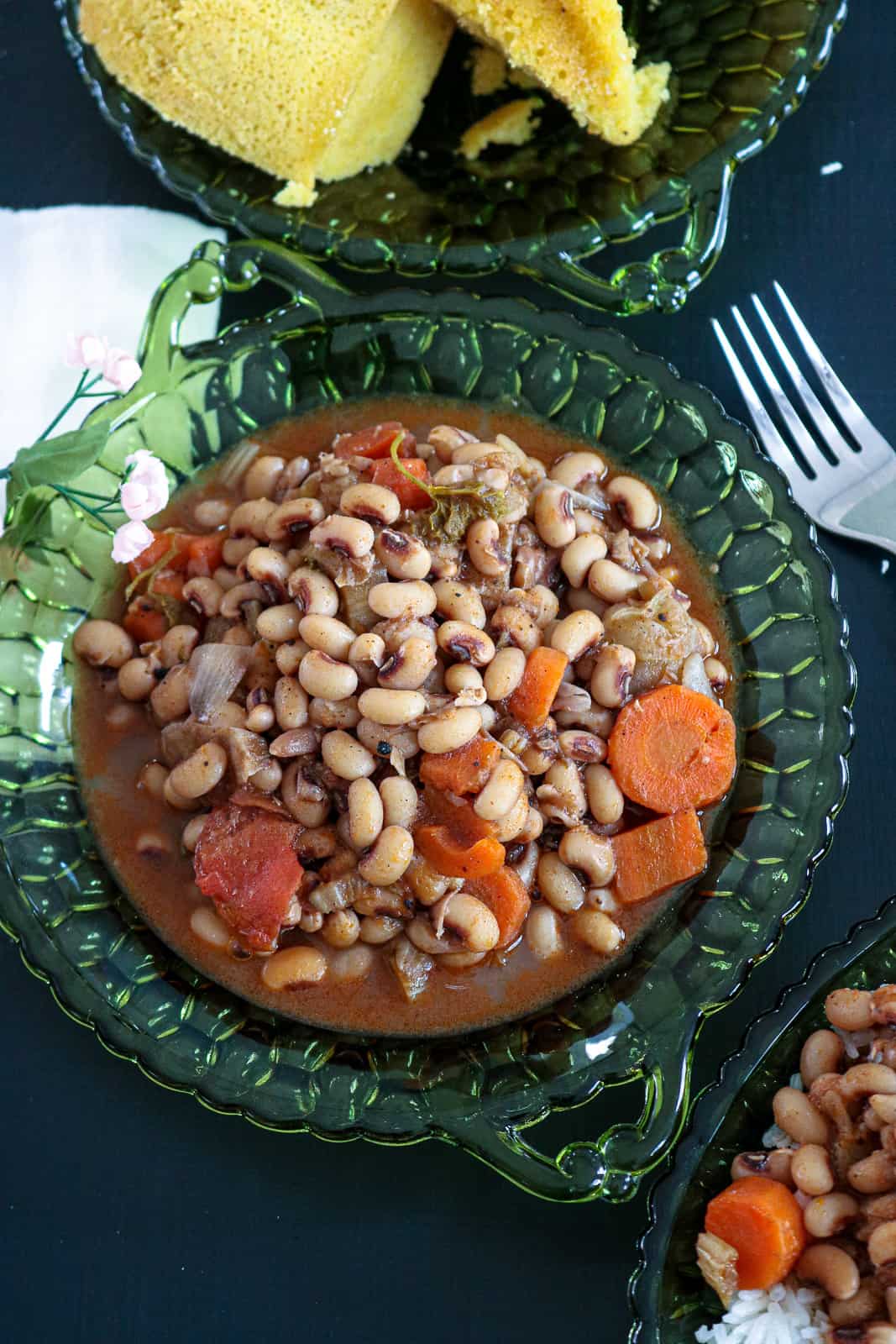 Black eye peas on green plate with fork on the side and corn bread