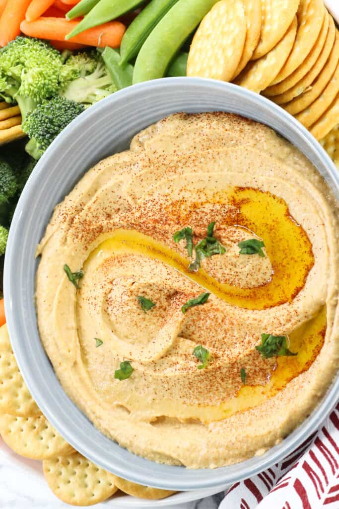 Hummus in gray bowl topped with olive oil and fresh herbs. 