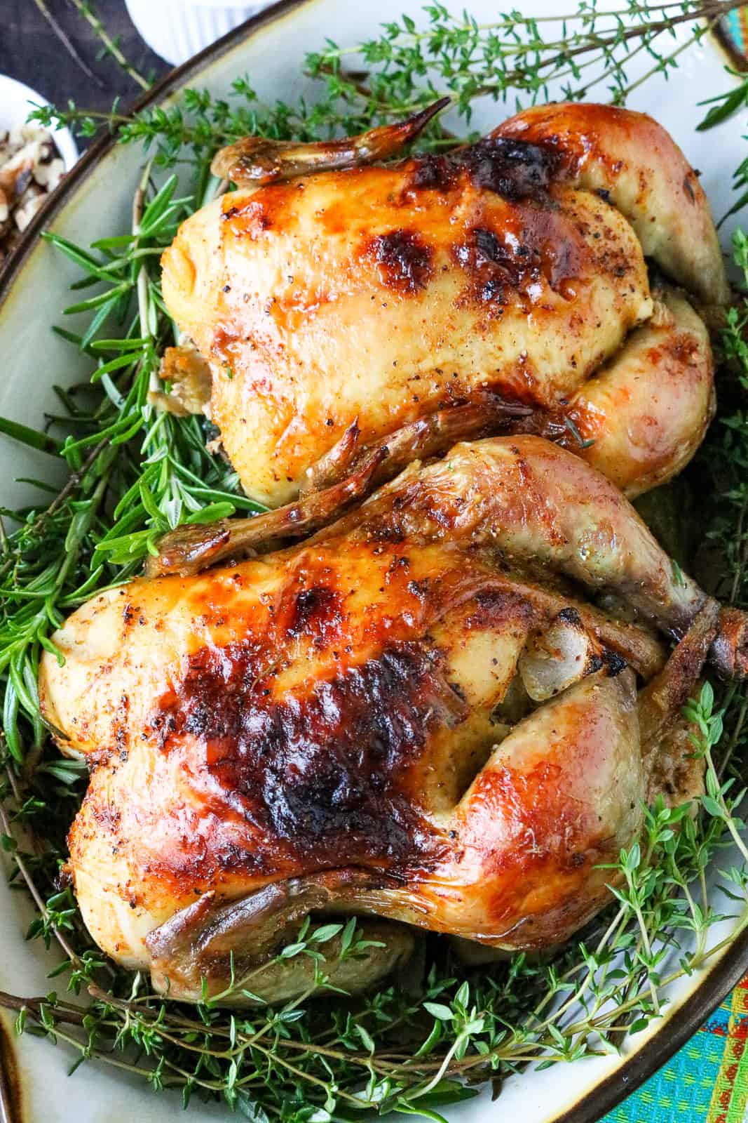 two Cornish Hens on a bed of fresh herbs in baking dish