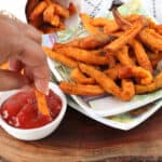 hand dipping fries in ketchup on wooden cutting obard
