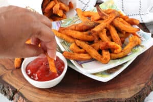 hand dipping fries in ketchup on wooden cutting obard