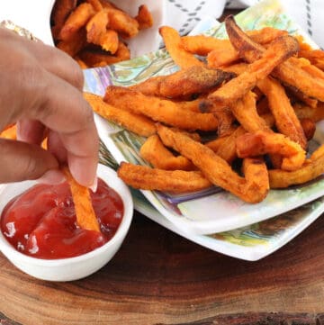 hand dipping fries in ketchup on wooden cutting obard