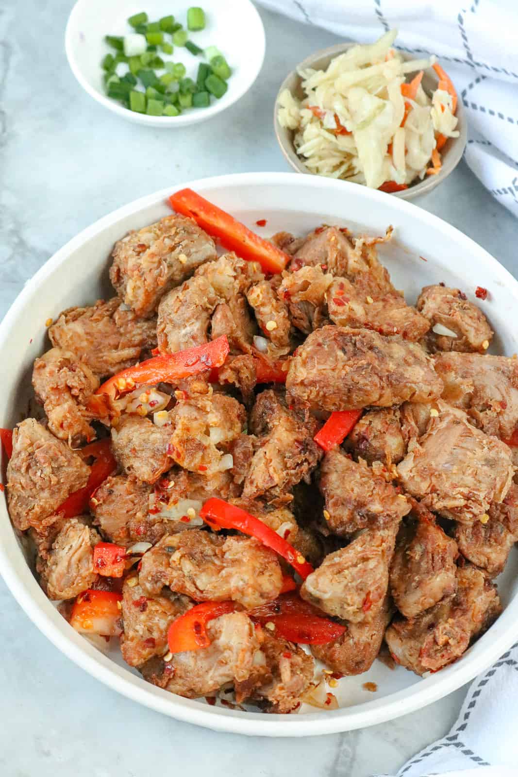 overhead picture of Haitian Griot recipe topped with red bell pepper slices and green onions with Pikliz in the background