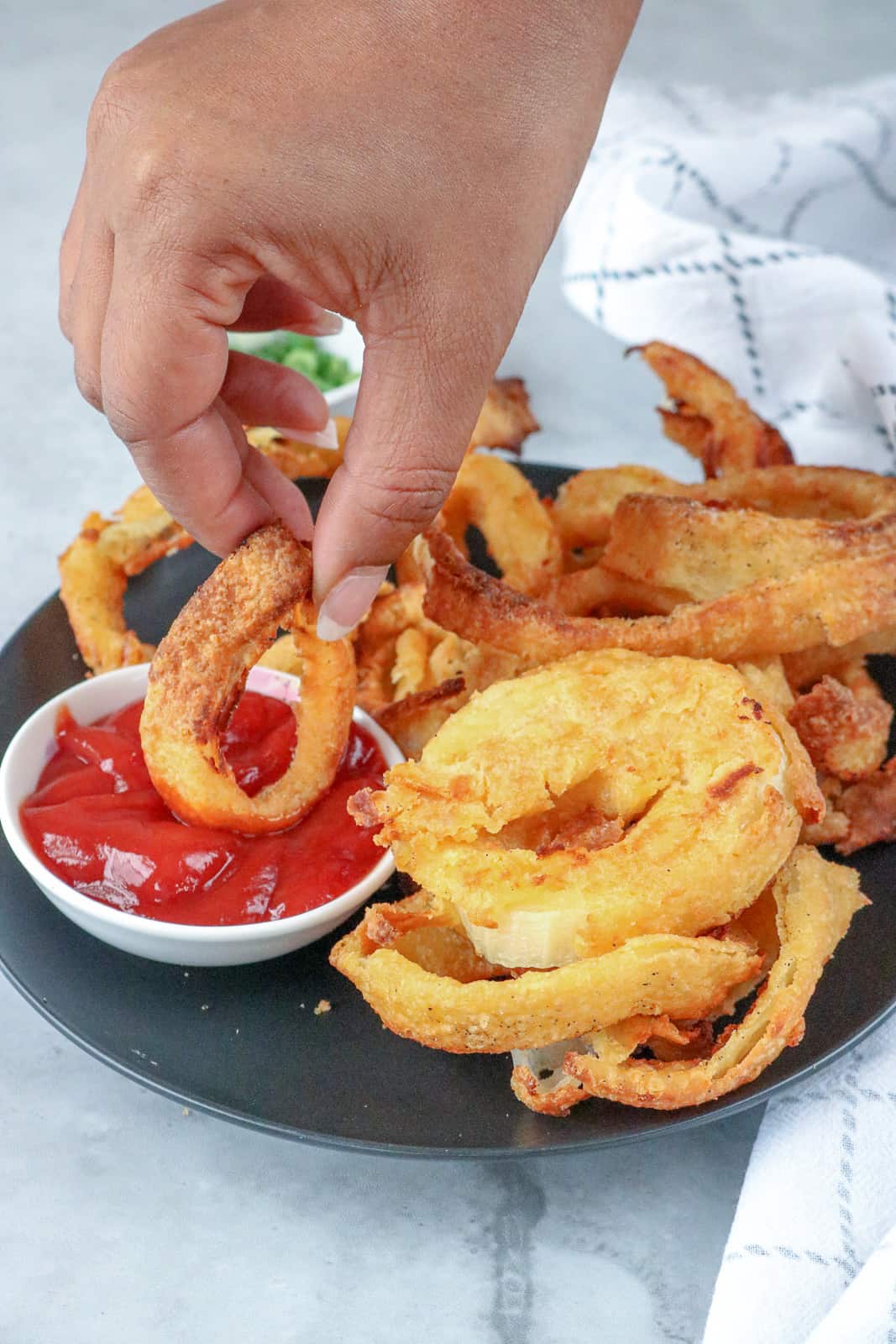 Hand dipping onion ring in ketchup