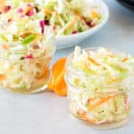 Haitian pikliz in two clear jars with pikliz on a plate in the background with spicy copper on a gray board