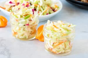 Haitian pikliz in two clear jars with pikliz on a plate in the background with spicy copper on a gray board