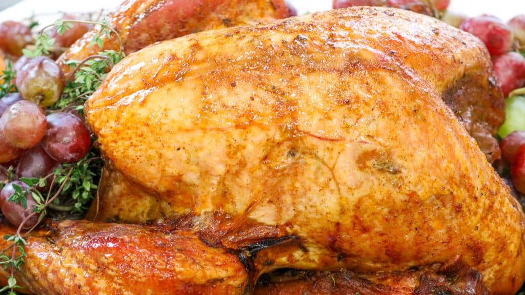Whole turkey on a bed of grapes, apples, fresh herbs on a white platter